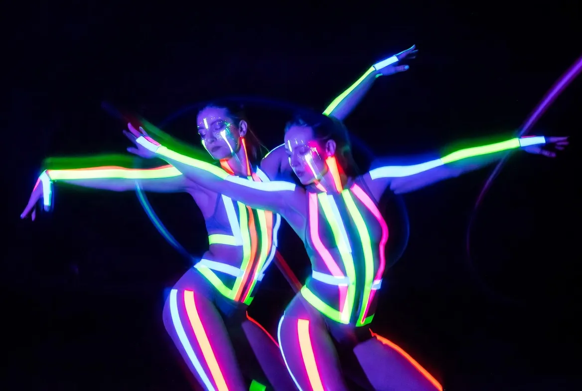 רקדניות ניאון בתלבושות UV זוהרות בחושך עם פסי אור ירוקים וורודים