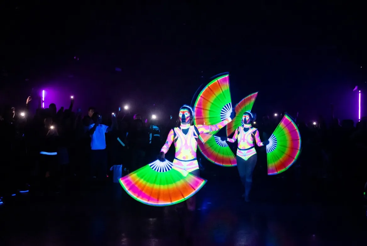 מופע ניאון UV בחושך — רקדניות עם תלבושות פלואורסצנטיות זוהרות בצבעים